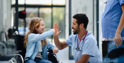 Doctor in scrubs giving a high five to a young girl in a wheelchair